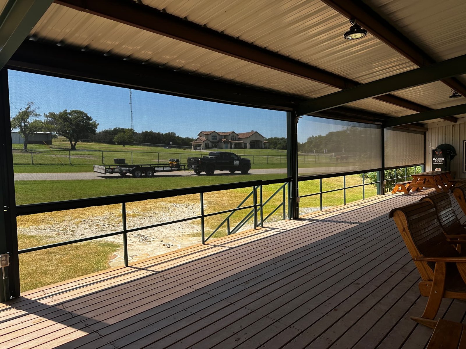 Retractable screens on a covered Texas ranch deck overlooking pasture, providing shade and insect protection while preserving the open view across the property.