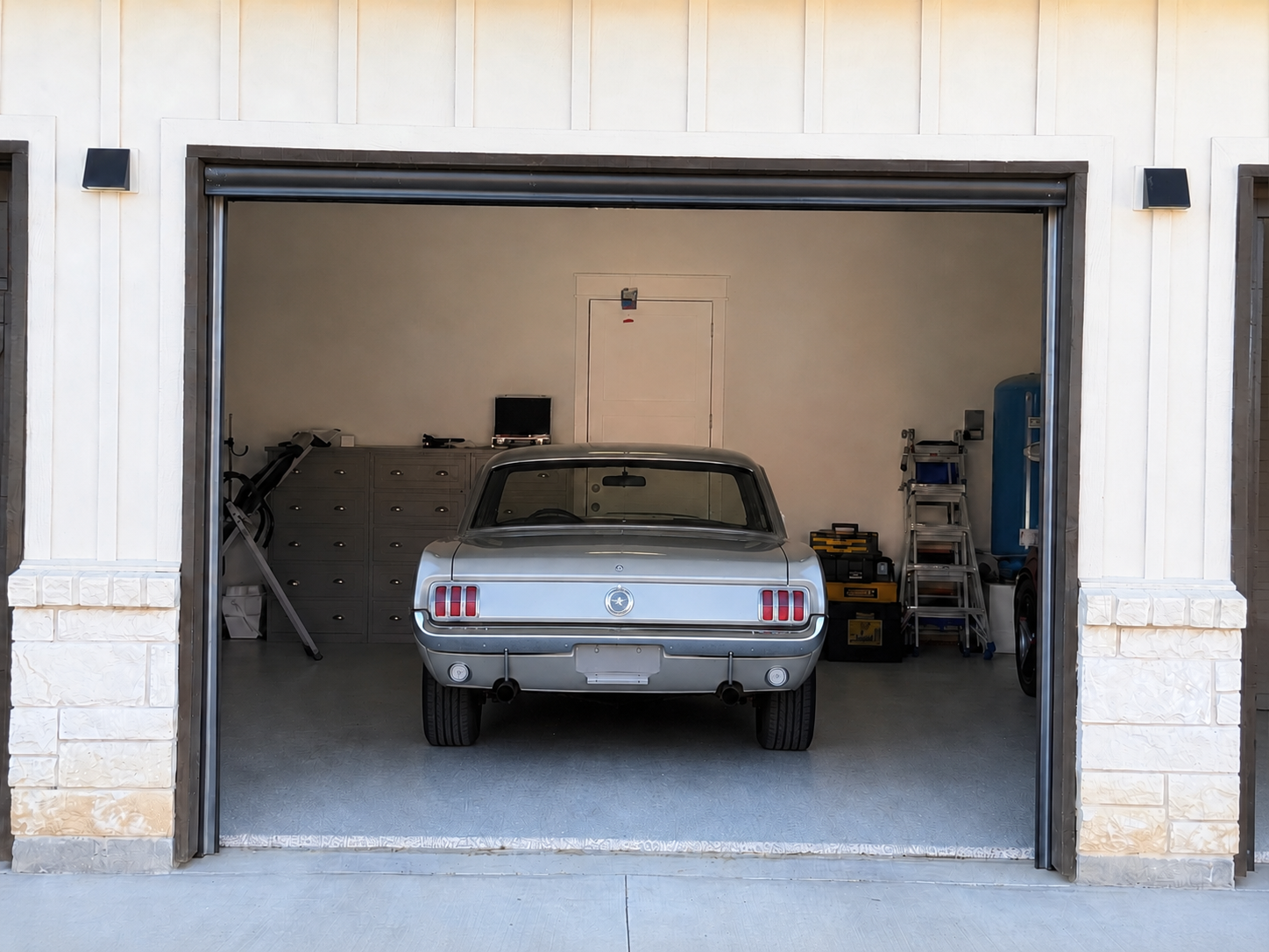A classic first-generation Mustang sits inside a garage, viewed from the exterior through fully lowered retractable garage door screens.
