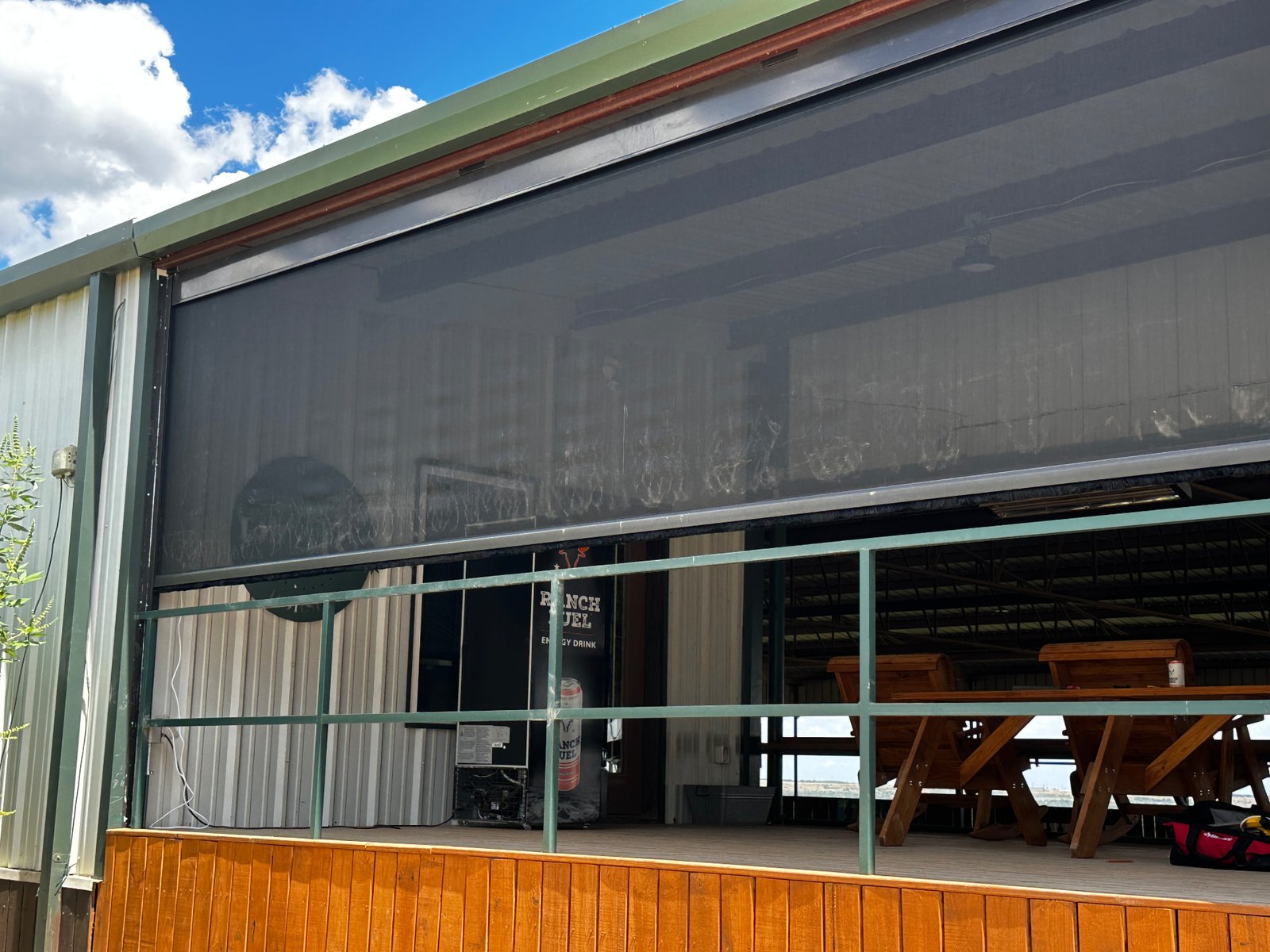 Large retractable screen partially lowered on a Texas ranch pavilion, providing shade and insect protection while keeping the outdoor space open.
