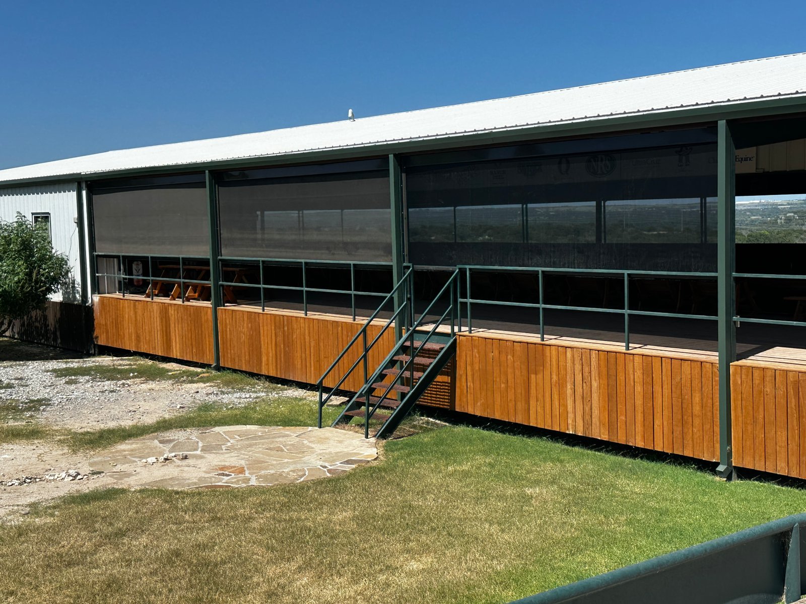 Retractable screens installed on a Texas ranch building with a wooden deck, creating a shaded and protected outdoor area while keeping the ranch setting visible.